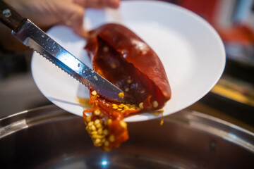 Hands pouring dry chili pepper seeds from plate into cooking pot