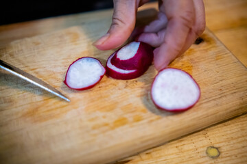 Hands slicing fresh radish on a cutting board