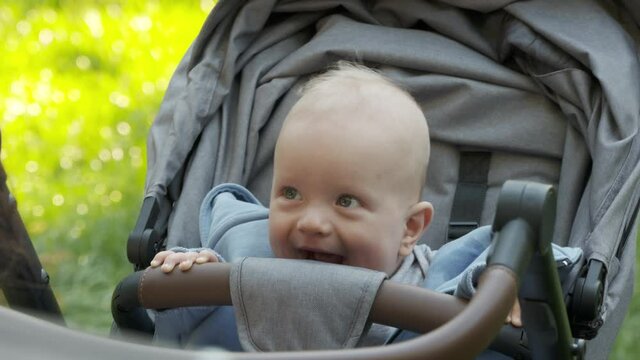 Face of happy baby boy sitting in baby stroller, cute caucasian six month old child outdoors. High quality 4k footage