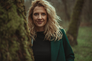 Naklejka premium Young blonde woman walking in the woods in a green coat
