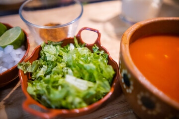 Clay bowls of chopped vegetables and delicious traditional Mexican pozole