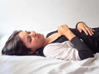 Obraz premium Young Brown Hair Peruvian Woman Lays on a White Sheet Bed Against Clear White Background