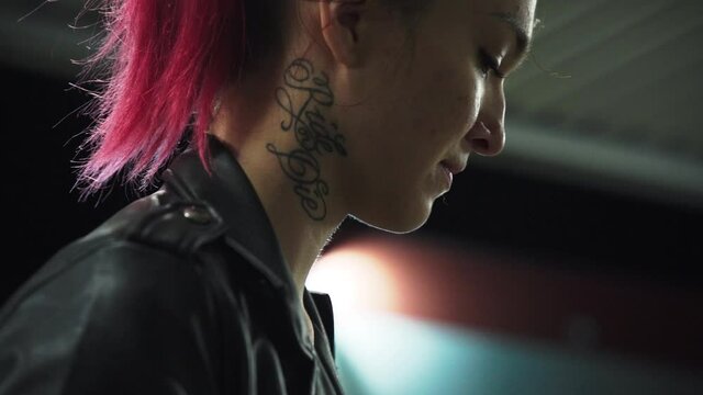 Emo red punk woman in black jacket with neck tattoo. Intentional soft focus