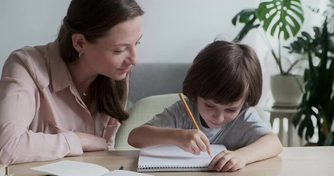 Little boy writing and drawing enthusiastically in notebook, mother supporting and helping. Teaching and hobbies together for mom or nanny and son. Development of abilities and creativity in children.
