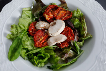 close up dish with lettuce salad, arugula, sun-dried tomatoes and white mushrooms. Vegetarian or vegan meal.