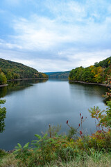 Fototapeta premium Pepacton Reservoir, Catskills, NY. Beautiful calm lake surrounded by forest. Colors of the leaves starting to change with the fall season. Selective focus on background. Blue sky, copy space.