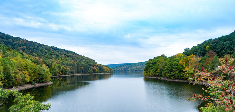Pepacton Reservoir, Catskills, NY. Beautiful calm lake surrounded by forest. Colors of the leaves are starting to change with the Autumn season, and reflections in the water. Blue sky, copy space.