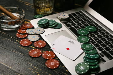 Laptop, poker chips and playing cards on dark wooden background