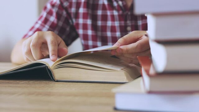 Close up and candid 4K of a man is reading textbook seriously on table with stacks of books as foreground in library. It shows concept of self learning and studying for education life.