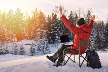 Adult man blogger or freelancer working on a laptop in winter forest. Freedom, remote work concept.