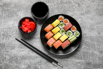 Plate with different sushi rolls, chopsticks and bowl with soy sauce on grunge background
