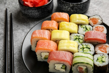 Plate with different sushi rolls and chopsticks on grunge background, closeup