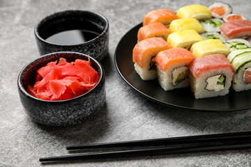 Plate with different sushi rolls, chopsticks and bowl with ginger on grunge table, closeup