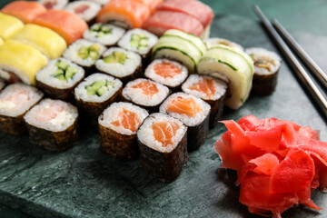 Board with set of delicious sushi rolls and ginger, closeup