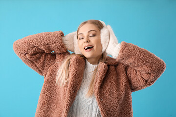 Happy woman in winter clothes and fur earmuffs on blue background