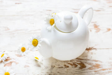 Obraz na płótnie Canvas Teapot and chamomile flowers on light wooden background, closeup