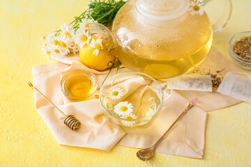 Teapot and cup of tasty chamomile tea, flowers and honey on color background