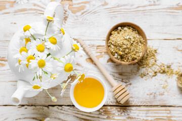 Fototapeta na wymiar Teapot of fresh chamomile tea with honey and flowers on light wooden background