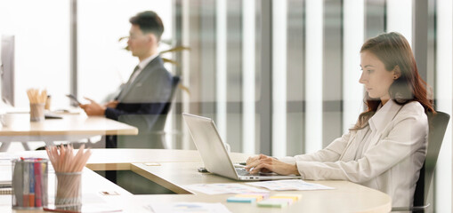 Happy millennial Caucasian female businesswoman employee officer staff in formal business suit sitting smiling look at laptop notebook computer screen joining webinar online remotely at company room