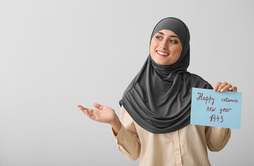 Young Muslim woman with greeting card for Islamic New Year on grey background