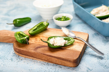 Board with uncooked jalapeno poppers on color background, closeup
