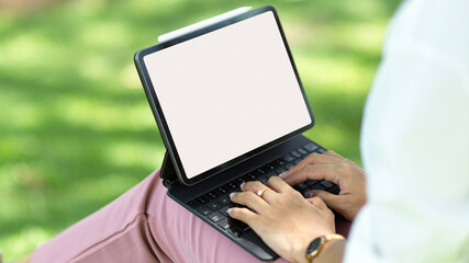 Female typing on portable tablet keyboard, sits in a park.