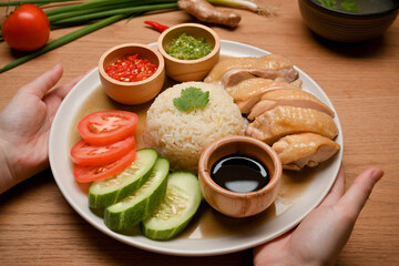 Close-up Female hands holding Hainanese chicken rice over the wooden table