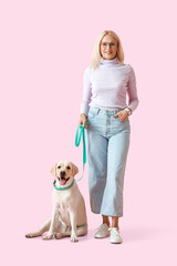 Mature woman with cute Labrador dog on pink background