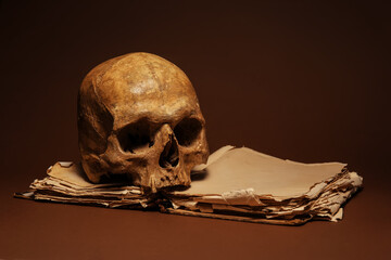 Human skull with old book on color background