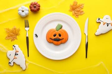 Stylish Halloween table setting with cookies on yellow background