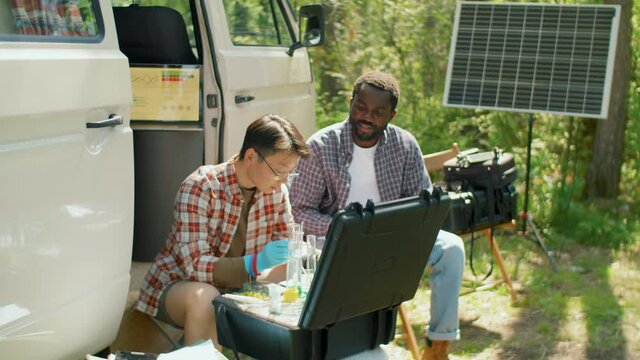 Horizontal handheld shot of two modern ethnically diverse ecologists doing chemical tests with samples and making notes