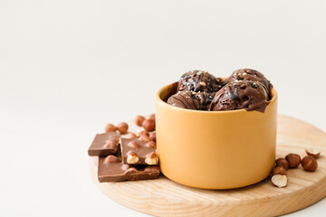 Bowl with delicious chocolate ice cream and hazelnuts on light background