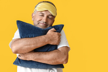 Mature man with sleep mask and pillow on color background