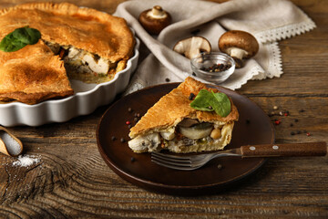 Baking dish and plate with piece of tasty chicken pot pie on wooden background