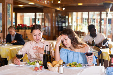 Portrait of two young women friends or lgbt couple having problems in relations, arguing in restaurant