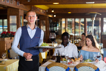 Portrait of confident waiter standing with salad and wine at restaurant