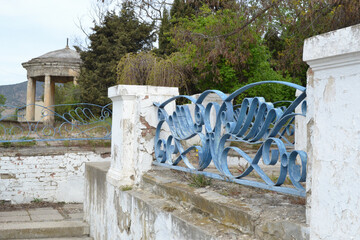 An old brick wall with a fence, white and blue, crumbling, masonry visible, nearby. In the...