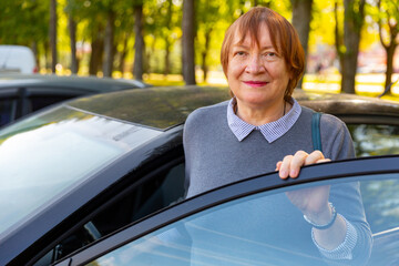 Positive mature woman standing beside her car and smiling. - Powered by Adobe