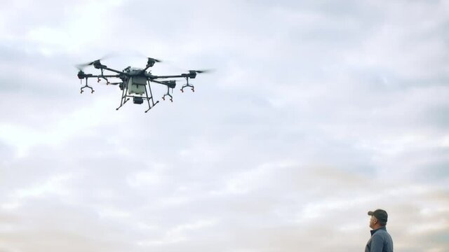 Farmer controlling a huge intelligent agriculture drone with spray nozzles near corn field early in the morning