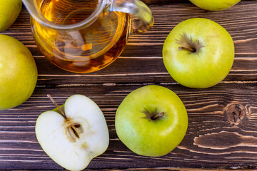 Green apples and jug with apple juice on wooden background