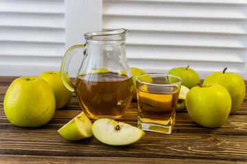 Green apples and jug with glass with apple juice on wooden background