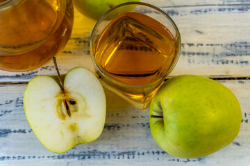 Green apples and jug with glass with apple juice on wooden background