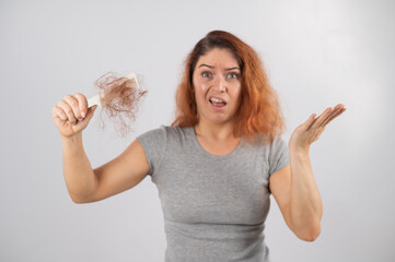 Caucasian woman with a grimace of horror holds a comb with a bun of hair. Hair loss and female...