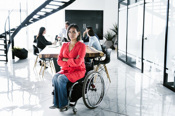 Portrait of latin transgender woman in wheelchair and people at meeting in the background in the...