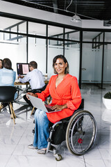 Latin transgender woman sitting in wheelchair in modern office using laptop with coworkers in Mexico City
