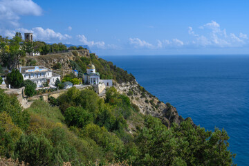 Fototapeta na wymiar View of the Black Sea and the ancient monastery on a picturesque rock covered with green plants on a sunny summer day. Golden domes glisten in the sun. Blue sky with white clouds. Crimea 