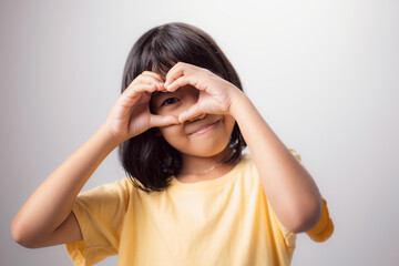 Healthy eyesight and eyes. Portrait of a smiling Asian kid with heart-shaped hands on his eyes. Smiling girl with glowing skin displaying a love symbol. Eye care is very important.