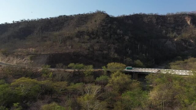 Aerial shot of Volkswagen combi driving on a desert mountain highway, with cactus and trees in Oaxaca, Mexico.