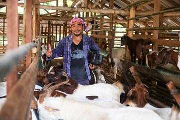 A farm worker or a farm owner raising young goats in a farmhouse. In the background, the goat pet stands and eats.