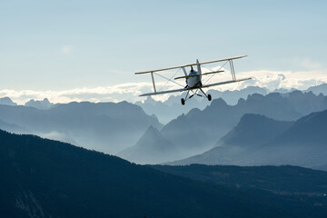 biplane plane flies over the mountains at sunset